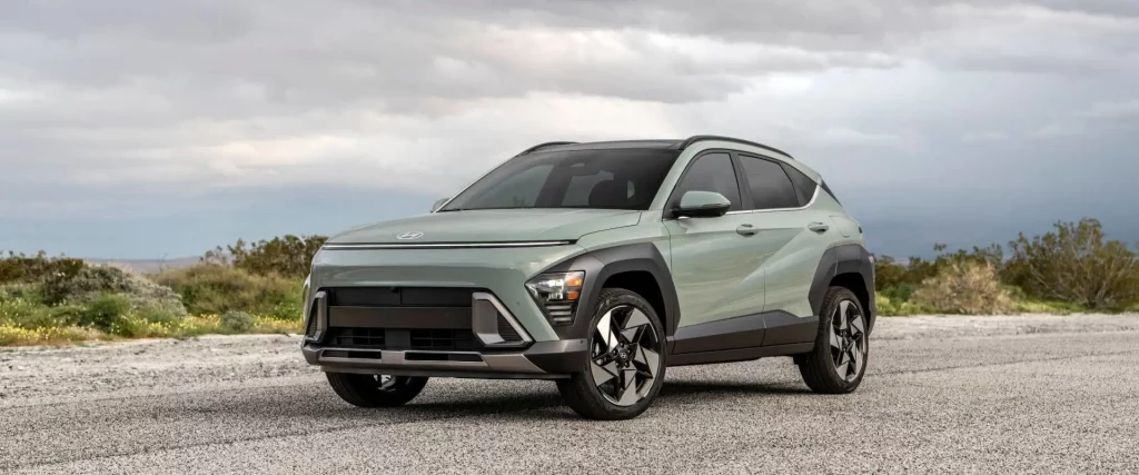 Hyundai Kona electric vehicle on a coastal road, with its distinctive teal color and sporty stance highlighting its compact SUV character.