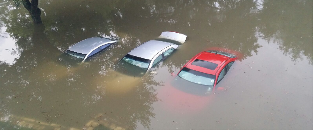 Multiple flooded cars submerged in standing floodwater in a parking lot after a storm