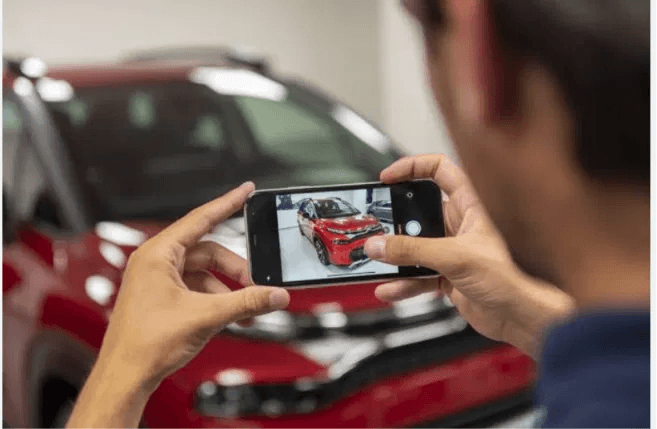 Person photographing a vehicle with a smartphone, the damage images that feed AI insurance claim decisions